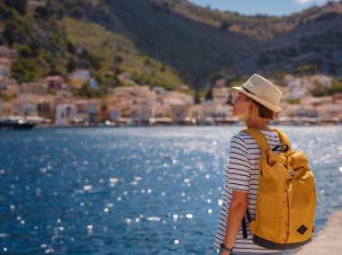 Sırt çantalı mutlu Asyalı kadın Symi Adaları 'nda tatilinin tadını çıkarıyor. Liman manzarası, Yunanistan 'ın Dodecanese kentindeki küçük bir ada, sakin bir atmosfer ve muhteşem bir mimari..
