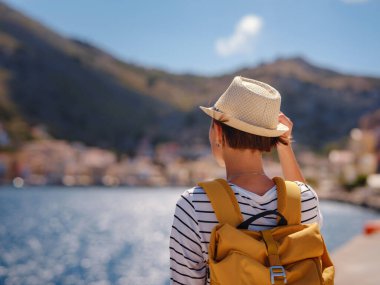 Sırt çantalı mutlu Asyalı kadın Symi Adaları 'nda tatilinin tadını çıkarıyor. Liman manzarası, Yunanistan 'ın Dodecanese kentindeki küçük bir ada, sakin bir atmosfer ve muhteşem bir mimari..