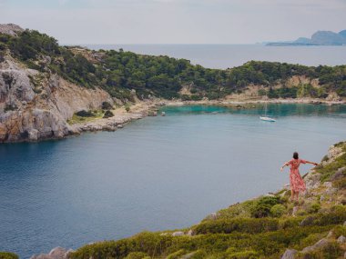 Şapkalı Asyalı kadın Akdeniz 'deki gök mavisi Bay manzarasına bakıyor. Seyahat ve tatil konsepti. Anthony Quinn körfezi, Yunanistan 'ın Rodos adasında berrak suyla birlikte. En güzel kumsal.