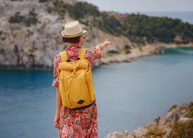 Şapkalı Asyalı kadın Akdeniz 'deki gök mavisi Bay manzarasına bakıyor. Seyahat ve tatil konsepti. Anthony Quinn körfezi, Yunanistan 'ın Rodos adasında berrak suyla birlikte. En güzel kumsal.