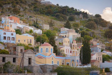 Symi Adası, Yunanistan. Yunanistan, Ege Denizi 'ndeki Rodos adalarından tatil yapıyor. Günbatımında bir Yunan adasının yamaçlarında renkli neoklasik güzel evler. Tatil seyahat arkaplanı.