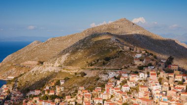 Symi Adası, Yunanistan. Yunanistan, Ege Denizi 'ndeki Rodos adalarından tatil yapıyor. Günbatımında bir Yunan adasının yamaçlarında renkli neoklasik güzel evler. Tatil seyahat arkaplanı.