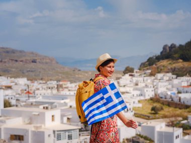 Ulusal Yunan bayrağıyla gezen genç bir kadın Lindos 'un keyfini çıkarıyor. Yunanistan 'a seyahat, Akdeniz adaları turizm sezonu dışında.