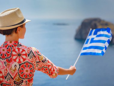 Yunan Adaları 'nda güneşli bir günün tadını çıkaran güzel mutlu kadın. Yunanistan 'a seyahat, turizm sezonu dışında Akdeniz adaları. Ulusal Yunan bayrağıyla gezen genç kadın deniz manzarasının keyfini çıkarıyor