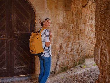 Yunanistan 'ın Rodos adasına yaz gezisi. Çizgili tişörtlü ve şapkalı genç Asyalı kadın Şövalyeler Kalesi 'nde yürüyor. Bayan gezgin Güney Avrupa 'yı ziyaret ediyor. Unesco Dünya Mirası Bölgesi