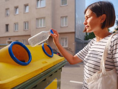 Avrupa caddesinde plastik şişe geri dönüşüm kutusu satan bir kadın. Dünyayı ve çevre bakımını kurtarmak için çöp kutusuna atılmadan önce atık ayıklama çöplüğü. Kirlilik çöpü geri dönüşüm yönetimi kavramı