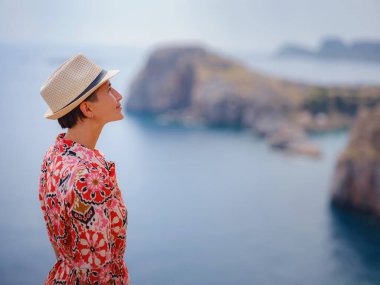 Yunan Adaları 'nda güneşli bir günün tadını çıkaran güzel mutlu kadın. Yunanistan 'a seyahat, turizm sezonu dışında Akdeniz adaları. Hayatın tadını çıkarmak ve denize bakmak. Turkuaz deniz arkaplanı.