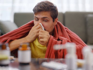 Kafkasyalı, burnu akan, elinde kağıt peçetelerle evde oturan genç bir adam. Hasta adam şiddetli bir soğuk algınlığına yakalandı. Semptomlar gösteriyordu. Ya da virüs hastalığına yakalandı.