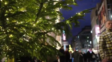Düsseldorf, Almanya - 13 Aralık 2022: Sokakta süslenmiş Noel ağacı, insanlar Dusseldorf 'taki ünlü alışveriş caddesi Schadowstrasse' nin Noel hediyelerini aramak için geçiyorlar.