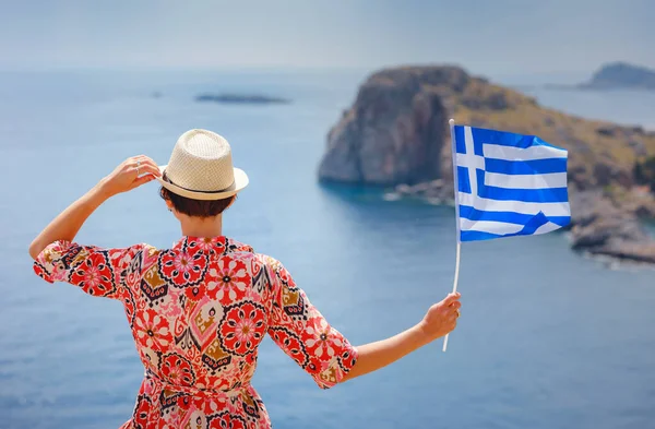 希腊群岛上快乐快乐的女性享受阳光日 前往希腊 地中海岛屿旅游旺季以外 年轻的女旅行家 举着希腊国旗欣赏大海 图库图片