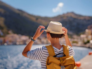 Sırt çantalı mutlu Asyalı kadın Symi Adaları 'nda tatilinin tadını çıkarıyor. Liman manzarası, Yunanistan 'ın Dodecanese kentindeki küçük bir ada, sakin bir atmosfer ve muhteşem bir mimari..