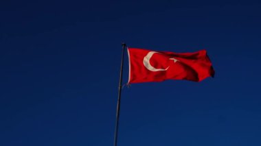 large bright flag of Turkey flutters on flagpole high above ground against backdrop of blue sky and clouds. Fethiye, Mugla Province