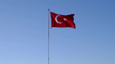 large bright flag of Turkey flutters on flagpole high above ground against backdrop of blue sky and clouds. Fethiye, Mugla Province