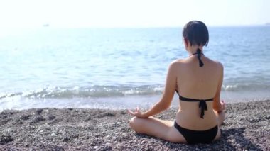 Yaz havası, Türk Rivierası 'nda deniz kenarında dinlenme. Mutlu genç Asyalı kadın deniz kıyısında meditasyon yapıyor. Gün doğumunda sahilde yoga yapan bir kadın. Sığ DOF kopya uzay arkaplanı.