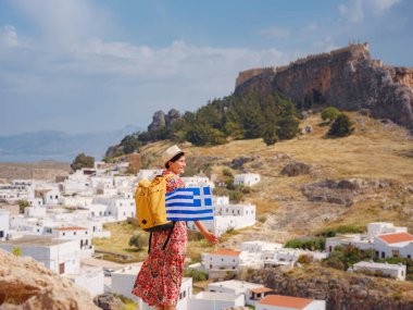 Ulusal Yunan bayrağıyla gezen genç bir kadın Lindos 'un keyfini çıkarıyor. Yunanistan 'a seyahat, Akdeniz adaları turizm sezonu dışında.