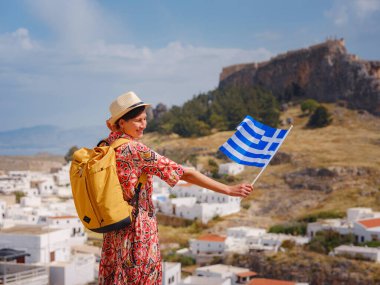 Ulusal Yunan bayrağıyla gezen genç bir kadın Lindos 'un keyfini çıkarıyor. Yunanistan 'a seyahat, Akdeniz adaları turizm sezonu dışında.