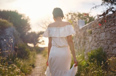 Çiçek tarlasında beyaz elbiseli güzel bir Asyalı genç kadın. Temiz havayı kucaklamak ve açık hava aktivitelerine katılmak. Friluftsliv konsepti, dışarıda mümkün olduğunca çok zaman geçirmek demektir.