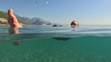 Seyahat ve tatil konsepti. Tatildeki genç erkek, Antalya 'nın berrak su sahillerinde yüzmenin keyfini çıkarıyor. Kolları açık yüzen sakallı yakışıklı bir erkek. Rahatla ve sakinleş.