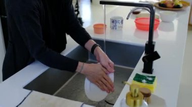 Beyaz, modern mutfakta ev ödevi yapan bir kadın. Mutfak lavabosunda bulaşık yıkayan ev kadınının ellerini kapat..