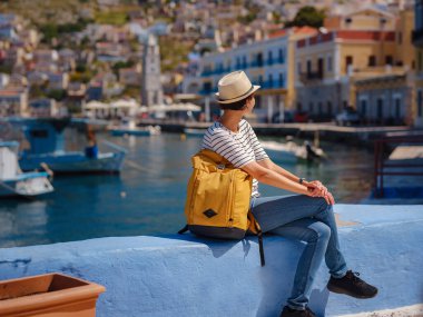 Sırt çantalı mutlu Asyalı kadın Symi Adaları 'nda tatilinin tadını çıkarıyor. Liman manzarası, Yunanistan 'ın Dodecanese kentindeki küçük bir ada, sakin bir atmosfer ve muhteşem bir mimari..
