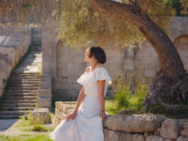 Beyaz elbiseli güzel Asyalı genç kadın. Rodos Akropolü. Stadyum ve tiyatro gibi çeşitli binalarla antik yerleşim yerlerinin ünlü kalıntıları..