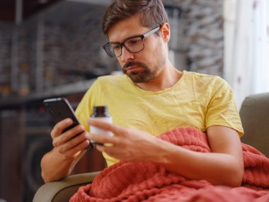 Genç beyaz adam okumak için akıllı telefon kullanıyor, ilaç reçetesini arıyor, internetten bilgi hakkında hap etiketi metni yazıyor, talimatlar yan etkiler, eczane tıbbı konsepti