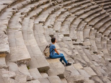 Amfitiyatroda oturan kadın turist yalnızlığın tadını çıkarıyor. Türkiye 'nin Antalya kıyısındaki Antik Kenti' ne düşük turizm sezonunda gitmek. Türkiye 'nin Yan Kenarı' ndaki antik tiyatro veya amfitiyatro manzarası.