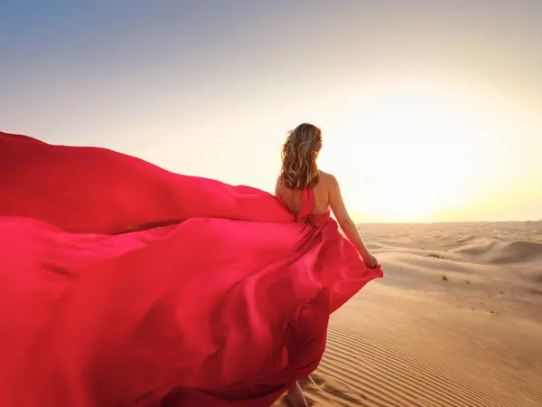 Desert adventure. Young arabian Woman in red silk dress in sands dunes of UAE desert at sunset, fantastic view. The Dubai Desert Conservation Reserve, United Arab Emirates.