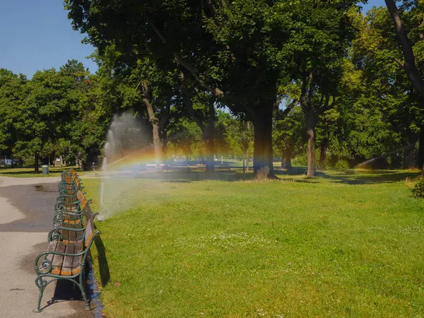 Rainbow on sprinkling machine watering grass in urban park in Vienna Austria.