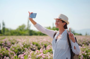 Kadın aromanın tadını çıkarıyor ve güneşli yaz gününde Şam Tarlası güllerinde akıllı telefonuyla fotoğraf çekiyor. Türkiye 'nin Isparta bölgesindeki Guneykent köyü eko-turizm için gerçek bir cennet.