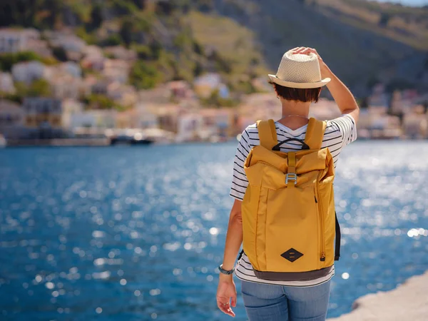 Sırt çantalı mutlu Asyalı kadın Symi Adaları 'nda tatilinin tadını çıkarıyor. Liman manzarası, Yunanistan 'ın Dodecanese kentindeki küçük bir ada, sakin bir atmosfer ve muhteşem bir mimari..
