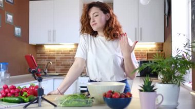 Ev mutfağındaki genç beyaz kadın salata yaparken kameraya tarif veriyor. Çevrimiçi yayın, yazar yemek pişirme konulu blog veya kursu yönetiyor.
