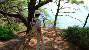 Seyahat tatilinde turist gezisi. Arkadan bak. Sırt çantalı bir dişi turist orman boyunca deniz boyunca yürüyor. Antalya 'da yaz seyahati