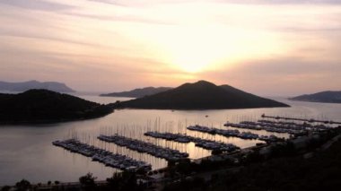 Akdeniz üzerinde gün batımları, Türkiye 'nin Kas kentindeki marinada teknelere altın parıltı saçıyor. Sahne huzurlu ve huzurlu bir akşam vaktidir. Limandaki pek çok lüks tekne ve yatın hava görüntüsü.