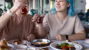 İki kadın yemek yerken gülüyor ve konuşuyor, açıkça görülüyor ki birbirlerinin arkadaşlığından keyif alıyorlar. Türk kahvaltısı, Pazar kahvaltısı veya feta peyniri ve yumurtalı brunch, restoranda Türk yemeği