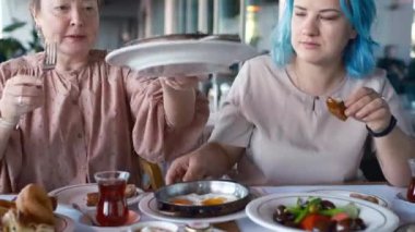 İki kadın yemek yerken gülüyor ve konuşuyor, açıkça görülüyor ki birbirlerinin arkadaşlığından keyif alıyorlar. Türk kahvaltısı, Pazar kahvaltısı veya feta peyniri ve yumurtalı brunch, restoranda Türk yemeği