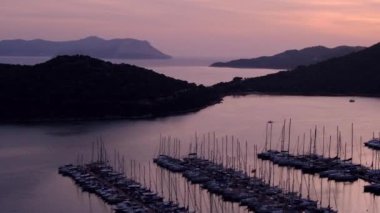 Akdeniz üzerinde gün batımları, Türkiye 'nin Kas kentindeki marinada teknelere altın parıltı saçıyor. Sahne huzurlu ve huzurlu bir akşam vaktidir. Limandaki pek çok lüks tekne ve yatın hava görüntüsü.