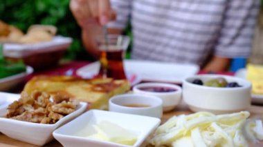 Kadınlar bahçede geleneksel Türk kahvaltısını seviyor. Etrafı yeşilliklerle çevrili bir masada oturuyor. Tabağında taze ekmek, peynir, zeytin, domates, salatalık, yumurta ve bal var. Bir fincan Türk çayı.