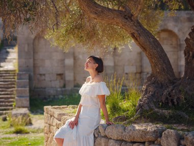 Beyaz elbiseli güzel Asyalı genç kadın. Rodos Akropolü. Stadyum ve tiyatro gibi çeşitli binalarla antik yerleşim yerlerinin ünlü kalıntıları..