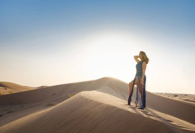 Çöl macerası. Gün batımında BAE çölünün kumullarında seksi boho mavisi bir elbise giyen genç Arap kadın. Dubai Çölü Koruma Alanı, Birleşik Arap Emirlikleri.