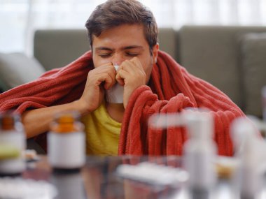 Kafkasyalı, burnu akan, elinde kağıt peçetelerle evde oturan genç bir adam. Hasta adam şiddetli bir soğuk algınlığına yakalandı. Semptomlar gösteriyordu. Ya da virüs hastalığına yakalandı.