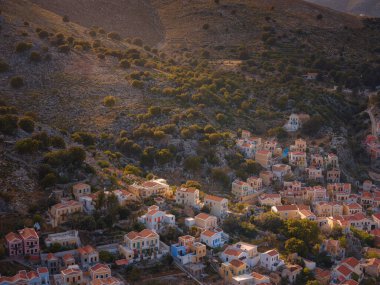 Symi Adası, Yunanistan. Yunanistan, Ege Denizi 'ndeki Rodos adalarından tatil yapıyor. Günbatımında bir Yunan adasının yamaçlarında renkli neoklasik güzel evler. Tatil seyahat arkaplanı.