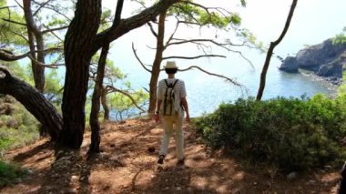 Seyahat tatilinde turist gezisi. Arkadan bak. Sırt çantalı bir dişi turist orman boyunca deniz boyunca yürüyor. Antalya 'da yaz seyahati