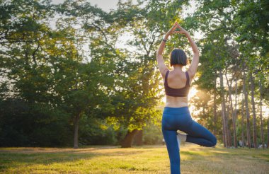 Genç Asyalı bir kadın sabah ya da akşam parkta yoga yapıyor sağlıklı bir kadın şehir parkında ağaç pozu veriyor. Farkındalık, kararlılık, sağlıklı alışkanlıklar ve denge konsepti