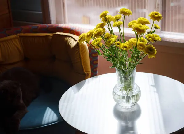 Flowers in interior design. Cozy home. Glass vase with beautiful flowers on table on window in room, space for text. bright sunlight lay on room