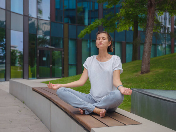Расслабься, расслабься. мирная работница-фрилансер, практикующая йогу, сидя в куче под стеклянными небоскребами после напряженного рабочего дня в офисе, держась за руки в мудре
