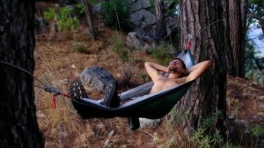 İki ağaç arasındaki yeşil hamakta dinlenen adam Türk Rivierası manzarasının tadını çıkarıyor. Akdeniz kıyısındaki dağların manzarası, çam ormanlarının manzarası