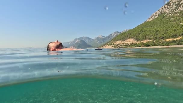 旅行和假期的概念 年轻的男性在假日里喜欢漂浮在安塔利亚清澈的海滩上 有胡子的英俊男子张开双臂游泳 轻松自在 — 图库视频影像