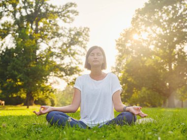Genç Asyalı bir kadın sabah veya akşam parkta meditasyon yapıyor sağlıklı bir kadın şehir parkında yoga yapıyor. Farkındalık, kararlılık, sağlıklı alışkanlıklar ve denge konsepti