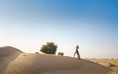 Çöl macerası. Gün batımında BAE çölünün kumullarında seksi boho mavisi bir elbise giyen genç Arap kadın. Dubai Çölü Koruma Alanı, Birleşik Arap Emirlikleri.